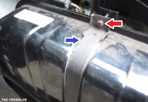 Красная стрелка указывает на болт, который необходимо снять, а синяя стрелка указывает на хомут, который необходимо разместить в нижней части багажного отделения после откручивания фиксирующего болта